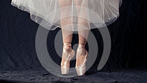 Close-up of dancing legs of ballerina wearing white pointe on a black background