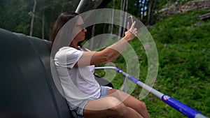 Close-up of a dark-haired middle-aged woman with dark glasses, she is on a ski lift, passing and taking pictures of