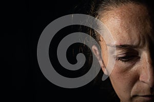 Close-up of a dark portrait of a very dimly lit woman. The woman has a frown and is looking down, conveying a feeling of sadness