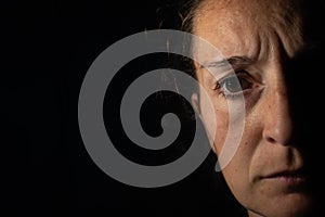 Close-up of a dark portrait of a very dimly lit woman. The woman has a frown and is looking at infinity, conveying a feeling of