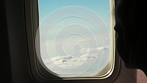 Close-up. dark silhouette of kid girl looking out through airplane`s window viewing Sky and Clouds and landscape below