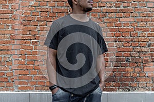 Close up of dark-skinned man in black blank T-shirt on bricked background.