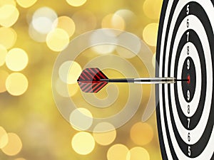 Close-up dart arrow hitting on target center on bullseye in wooden dartboard with blurred yellow gold lights bokeh background