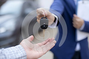 Close up of dealer giving key to new owner and shaking hands in auto show