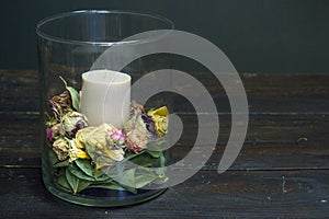 Close-up decor element glass vase with dry flowers and a candle inside on a wooden table, selective focus