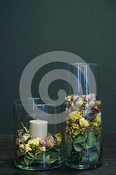 Close-up decor element glass vase with dry flowers and a candle inside on a wooden table, selective focus