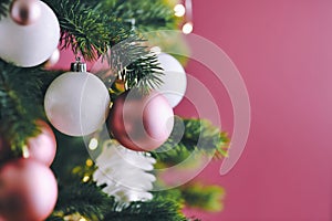 Close up of decorated Christmas tree with white seasonal and pink tree ornaments like baubles and stars on dark pink background