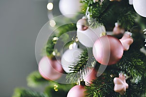 Close up of decorated Christmas tree with white seasonal and pink tree ornaments like baubles and stars on gray background