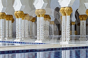 Close-up decorated marble columns on the top with like golden palm with reflected pool in front of Sheikh Zayed Grand Mosque