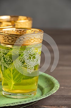 Close-up of decorated mint tea glasses, on green plate, selective focus, on dark wooden table, dark background