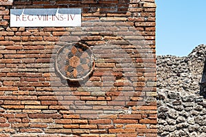 Close-up on stone sculpture representing a flower decorating old bricks wall of house in ruins in Pompei