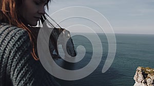 Close-up defocused young tourist woman meditating at epic nature scenery at Etretat, hair blowing in wind slow motion.