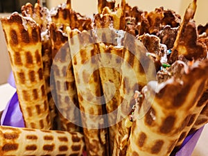 Close-up of delicious chocolate waffle rolls lie on white plate. Preparation of a sweet dessert. White clean kitchen and table.