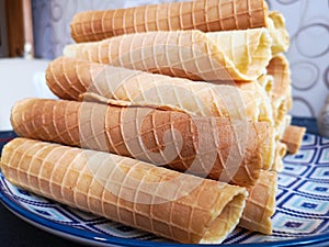 Close-up of delicious chocolate waffle rolls lie on white plate. Preparation of a sweet dessert. White clean kitchen and table.