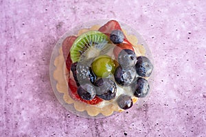 Close up of a delicious fruit tart with blueberries kiwi strawberries grapes and raspberries on a light purple background