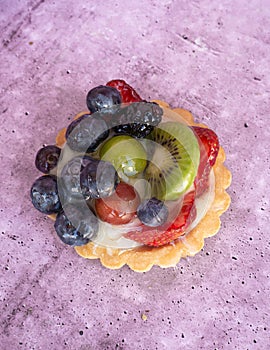 Close up of a delicious fruit tart with blueberries kiwi strawberries grapes and raspberries on a light purple background