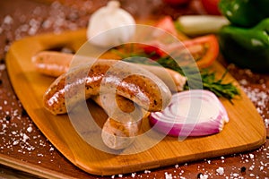 Close up of delicious grilled sausages and vegetables, tomato, onio, green pepper and rosemary spices on a wooden