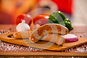 Close up of delicious grilled sausages and vegetables, tomato, onio, green pepper and rosemary spices on a wooden