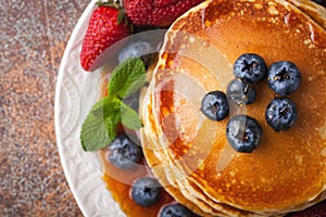 Close-up delicious pancakes, with fresh blueberries, strawberries and maple syrup on a rusty background. With copy space. Top view