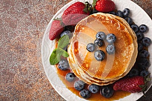 Close-up delicious pancakes, with fresh blueberries, strawberries and maple syrup on a rusty background. With copy space. Top view