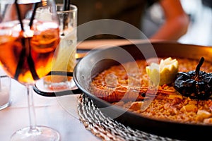 Close-up of delicious seafood valencia paella with king prawns, rice with spices in pan and Glass of aperol spritz cocktail long d