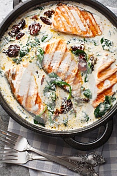 Close up of delicious tuscan cream salmon with spinach and sun-dried tomatoes in the pan on the table. Vertical top view