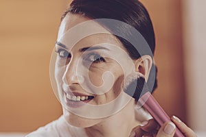 Close up of delighted woman powdering her face