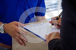 Close up Delivery man in blue uniform holding package while woman is signing receiving documents.