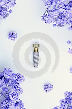 Close up of dental implant lying on white background among flowers.