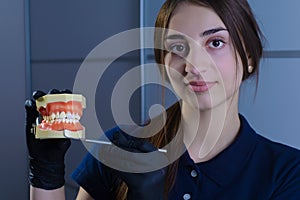 Close-up of a dentist doctor, smiling, wearing gloves, holding in his hand a dental instrument for examination, and a dummy of