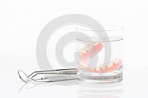 Close up of dentures in glass of water and dental tool with notice paper on white background