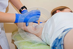 Close-up of depilation master`s hands in blue rubber gloves wiping a clientâ€™s armpit with a cotton pad.