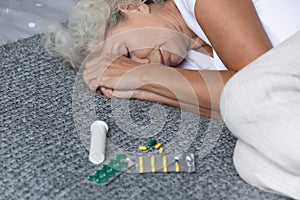 Close up depressed mature woman lying on bed with meds