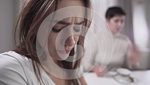 Close-up of depressed young brunette girl shaking when senior woman banging fist on table. Frightened adult daughter