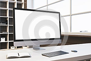 Close up of designer office desktop with empty white computer monitor, window with city view and wooden shelves in the background