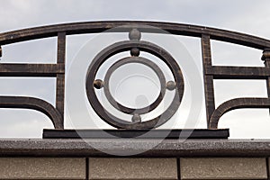 Close-up detail of beautiful vintage forged metal big dark abstract decoration on top of stone granite gray brown fence. Work of b