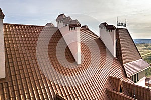 Close-up detail of building steep shingle roof and brick plastered chimneys on house top with metal tile roof. Roofing, repair and