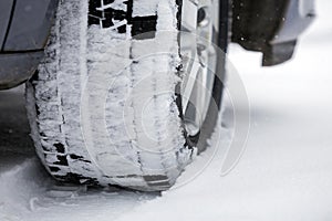 Close up detail car wheel with new black rubber tire protector on winter snow covered road. Transportation and safety concept