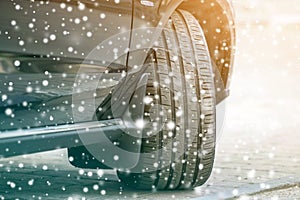 Close up detail car wheel with new black rubber tire protector on winter snow covered road. Transportation and safety concept