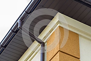 Close-up detail of cottage house corner with brown metal planks siding and roof with steel gutter rain system. Roofing,
