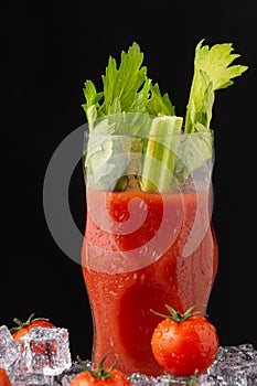 Close-up detail of crystal glass with bloody mary cocktail and celery, with ice cream and crerry tomatoes, on black background