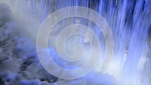 Close up detail of falling water in blue illuminated waterfall fountain at night