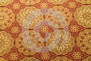 Close up of a detail or a fug or tapestry on the floor in yellow and orange and gold with circular patterns seen from above