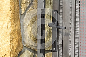 Close-up detail of limestone fence near residential house and closed iron gate door with lock and metal handle. Stone masonry, sec