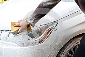 Close-up detail manual car wash with high pressure water equipment pump and soapy sponge at home backyard outdoor summer