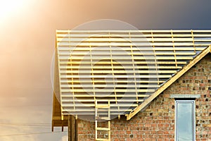 Close-up detail of new brick house top with two narrow plastic attic windows and wooden roof frame under construction on dark blue