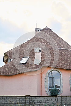 Close-up detail of new modern ecological cottage house top with shingled brown roof on blue sky background.