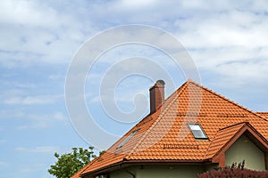 Close-up detail of new modern house top with shingled red roof, high chimney, attic windows on clear blue sky copy space backgroun