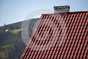 Close-up detail of new modern house top with shingled red roof and wooden sidings on foggy spruce mountains background.