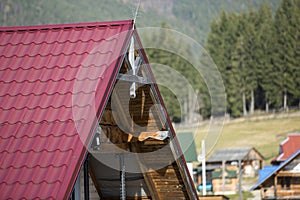 Close-up detail of new modern house top with shingled red roof and wooden sidings on foggy spruce mountains background.